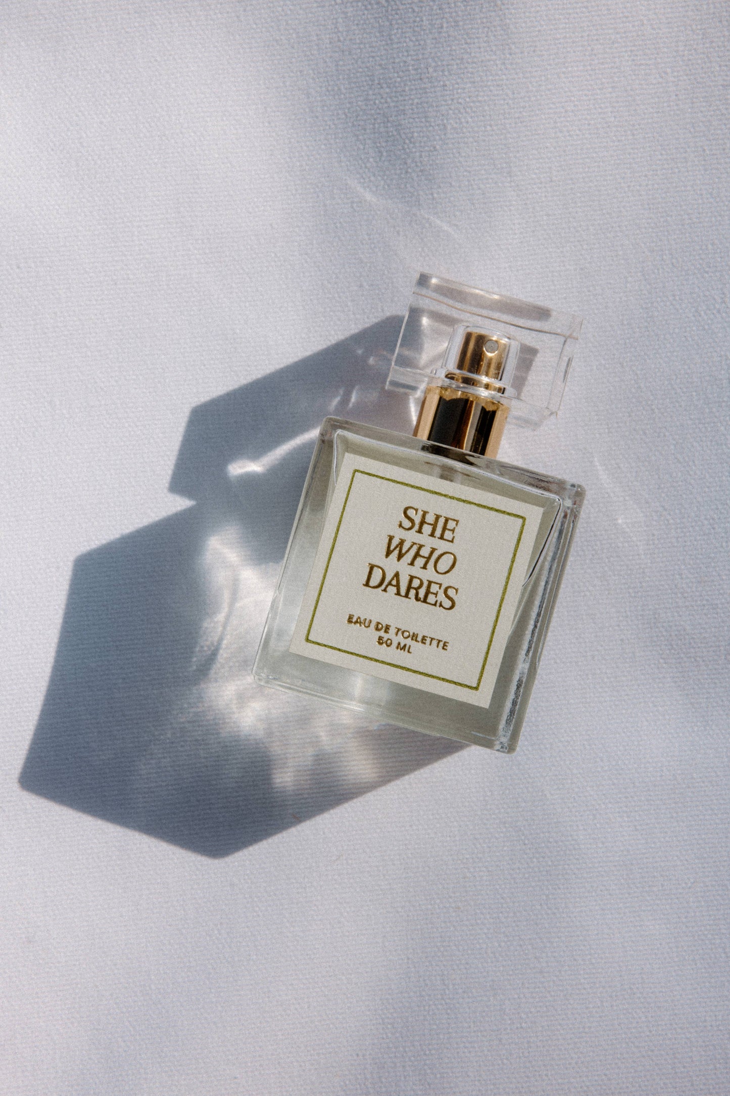 Perfume bottle labeled 'She Who Dares' on a light background
