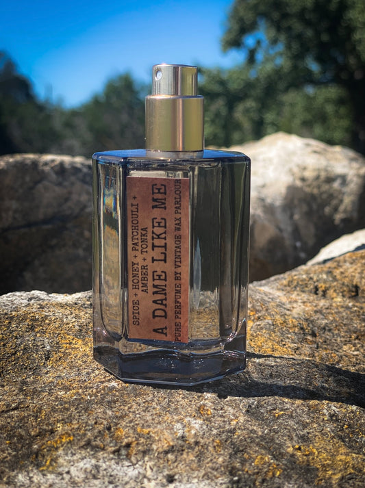 Perfume bottle labeled 'A Dame Like Me' on a stone surface with a natural background