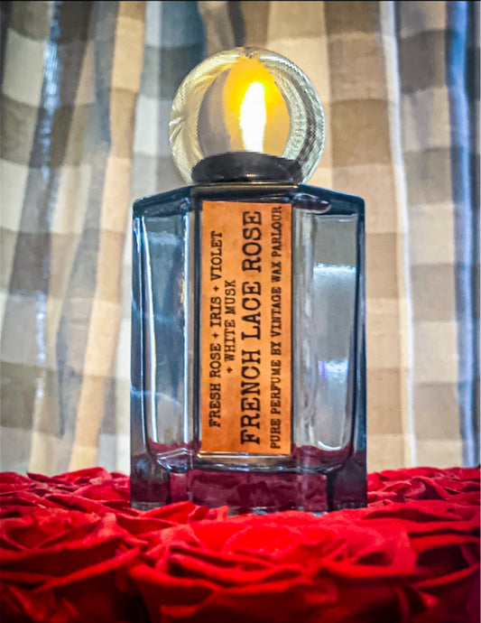 Perfume bottle labeled 'French Lace Rose' on a bed of red roses with a plaid curtain background